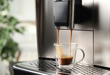 Photo of Espresso machine pouring coffee into glass cup against blurred background, closeup. Space for text