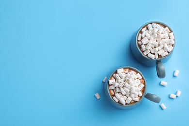 Photo of Delicious cocoa drink with marshmallows on light blue background, flat lay. Space for text