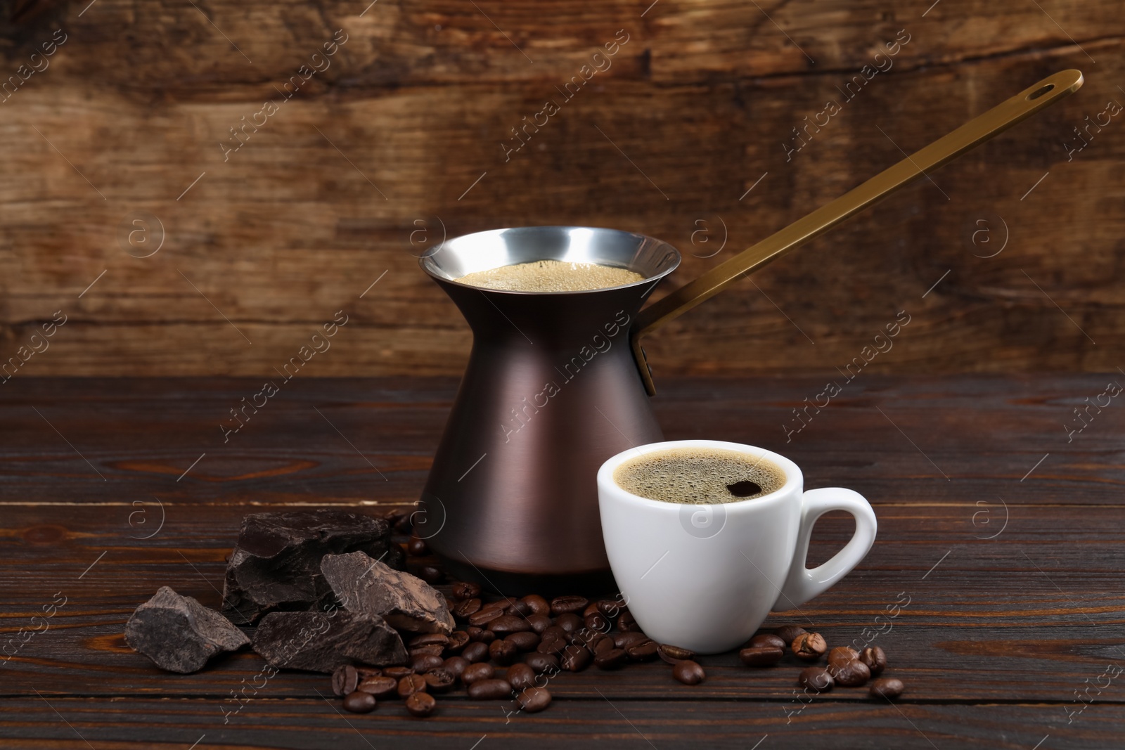 Photo of Hot turkish coffee pot, cup of drink, beans and chocolate on wooden table