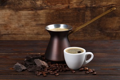 Photo of Hot turkish coffee pot, cup of drink, beans and chocolate on wooden table
