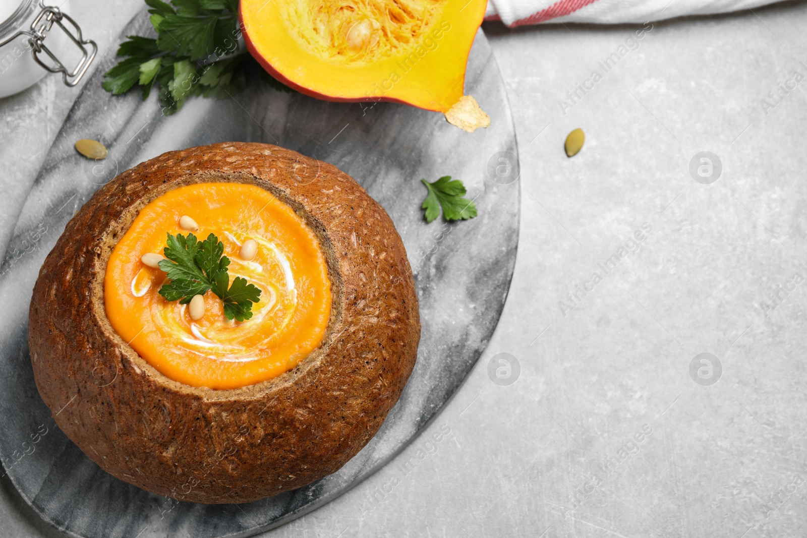 Photo of Tasty pumpkin cream soup in bread loaf on grey table, flat lay. Space for text