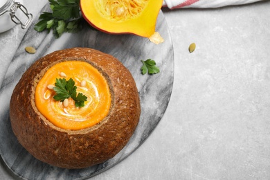 Photo of Tasty pumpkin cream soup in bread loaf on grey table, flat lay. Space for text