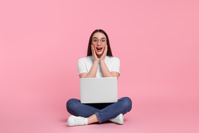 Photo of Surprised young woman with laptop on pink background
