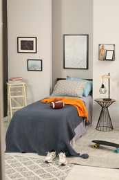 Photo of Stylish teenager's room interior with comfortable bed, lamp and American football ball