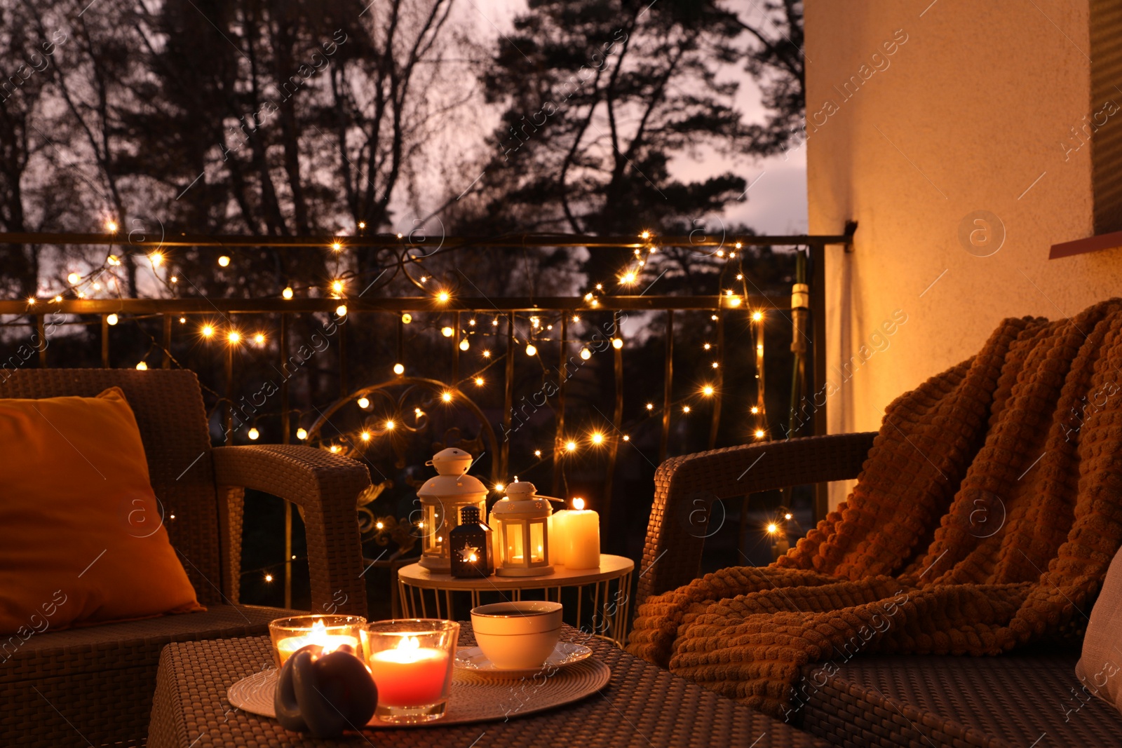 Photo of Beautiful view of garden furniture with pillow, soft blanket and burning candles at balcony