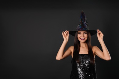 Photo of Beautiful woman wearing witch costume for Halloween party on black background, space for text