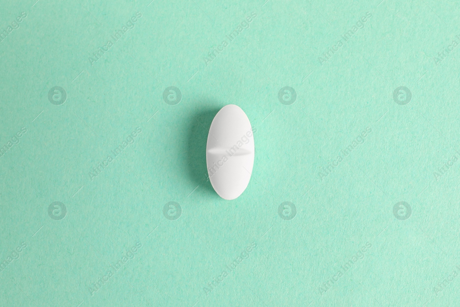 Photo of One white pill on green background, top view