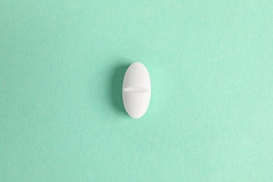 Photo of One white pill on green background, top view