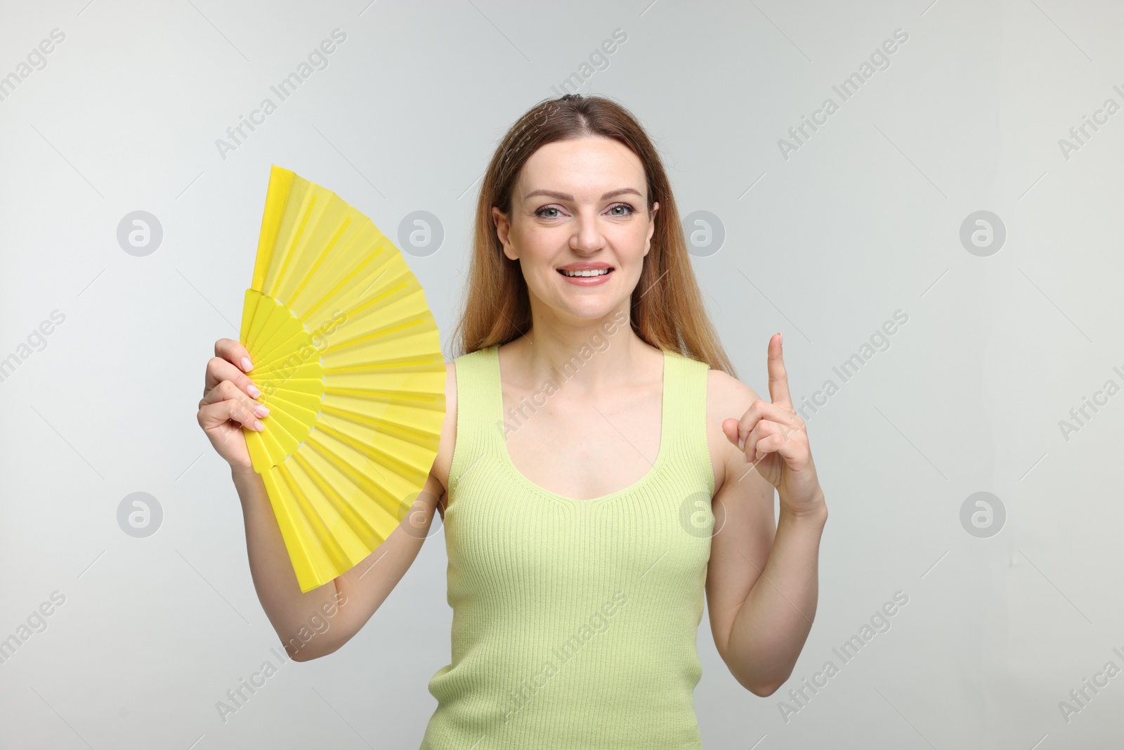 Photo of Happy woman with yellow hand fan pointing on light grey background