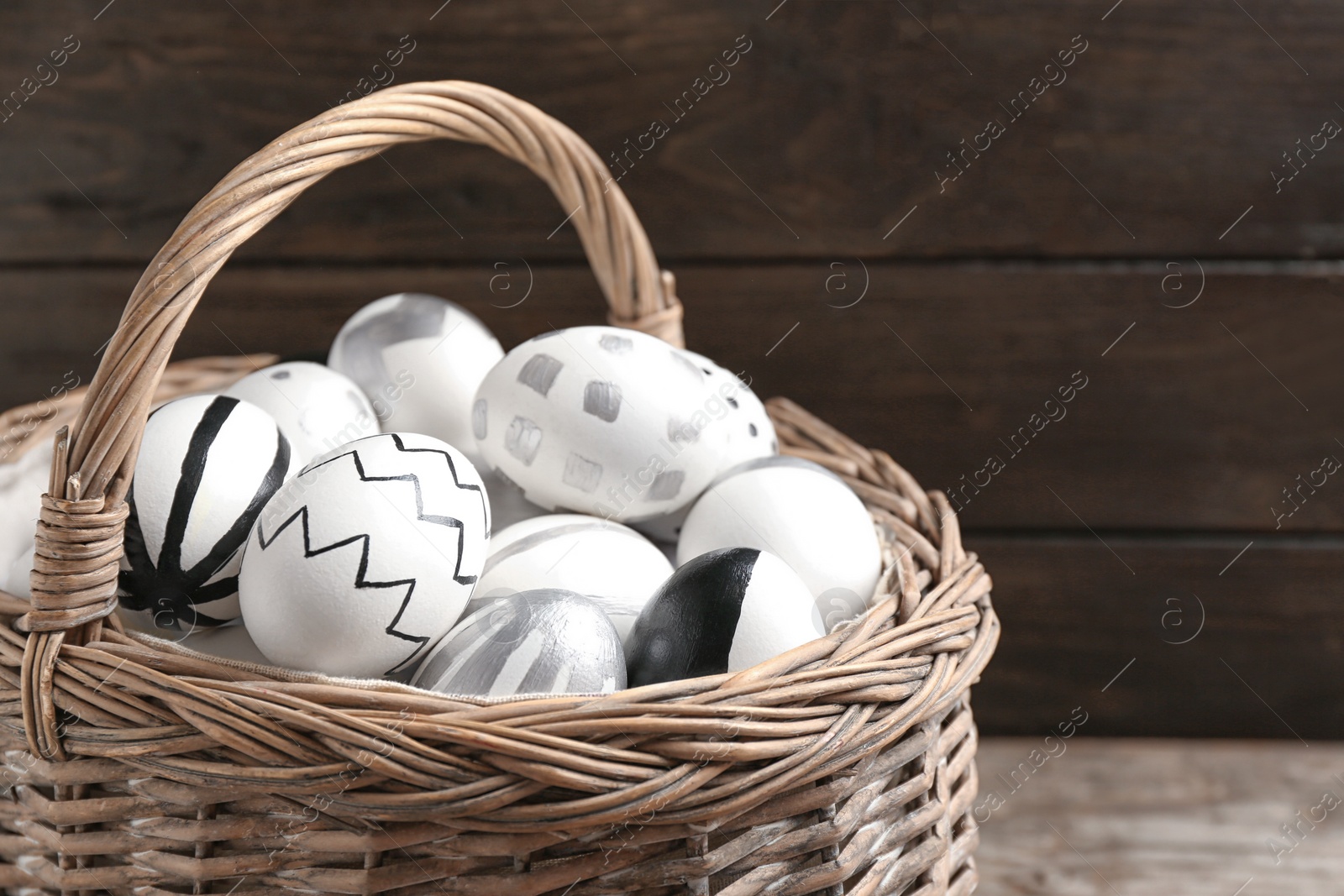 Photo of Basket of Easter eggs on wooden background, closeup. Space for text