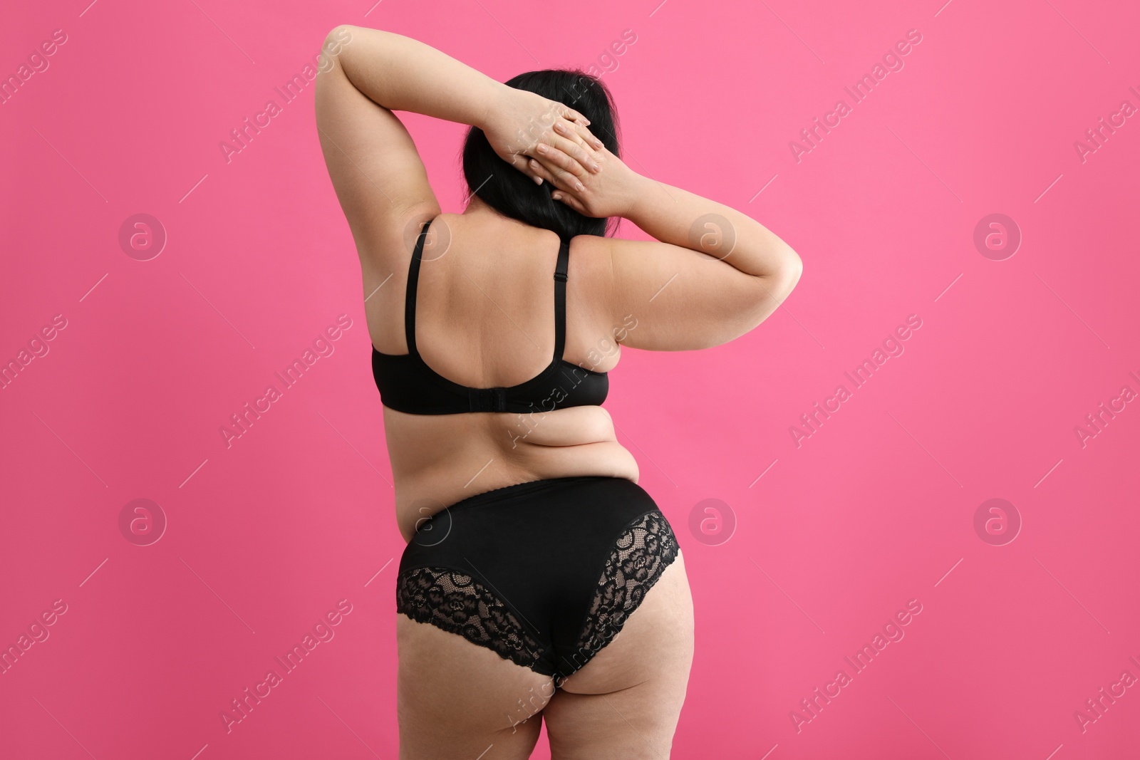 Photo of Back view of beautiful overweight woman in black underwear on pink background. Plus-size model