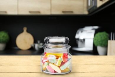 Image of Glass jar with tasty gummy candies on wooden table in kitchen