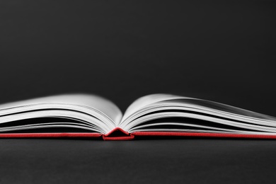 Photo of Open book with red cover on black background, closeup view