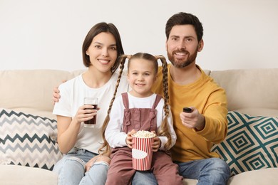 Photo of Happy family watching TV with popcorn on sofa indoors