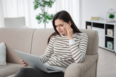 Photo of Young woman suffering from headache while sitting on sofa at home