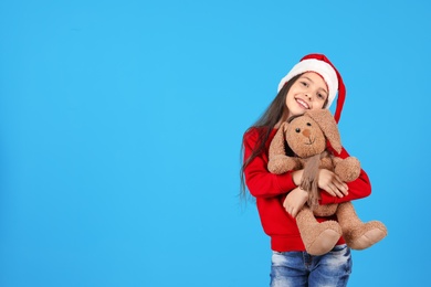 Cute little child in Santa hat with toy rabbit on color background. Christmas celebration