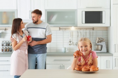 Photo of Little girl with freshly oven baked buns at table in kitchen