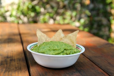 Delicious guacamole made of avocados and nachos on wooden table outdoors, space for text