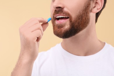 Photo of Man taking pill on beige background, closeup