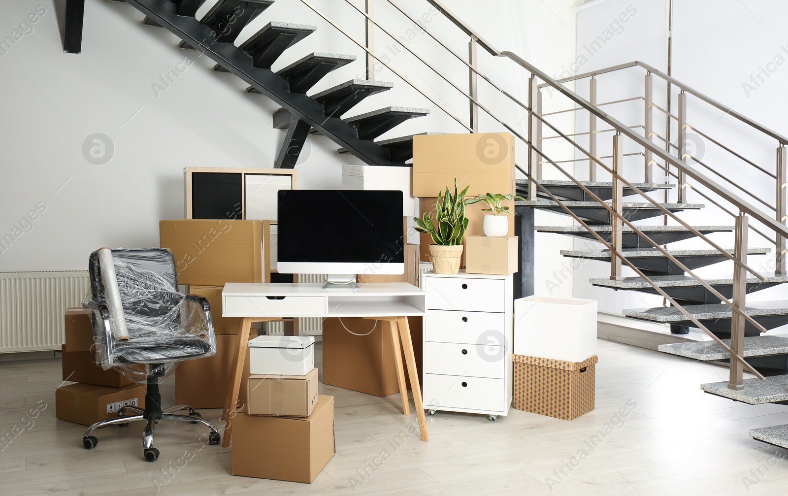 Photo of Cardboard boxes and furniture near stairs in office. Moving day