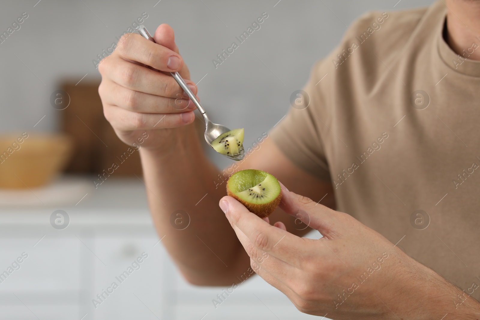 Photo of Man eating kiwi with spoon on blurred background, closeup