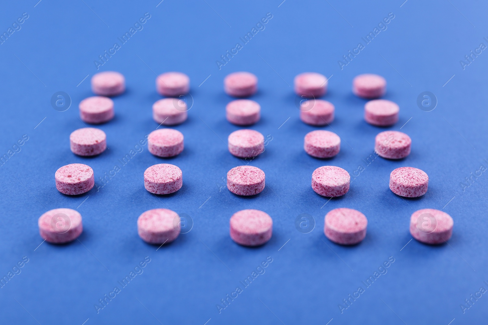 Photo of Many pink vitamin pills on blue background, closeup