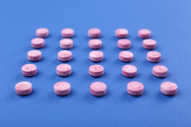 Photo of Many pink vitamin pills on blue background, closeup