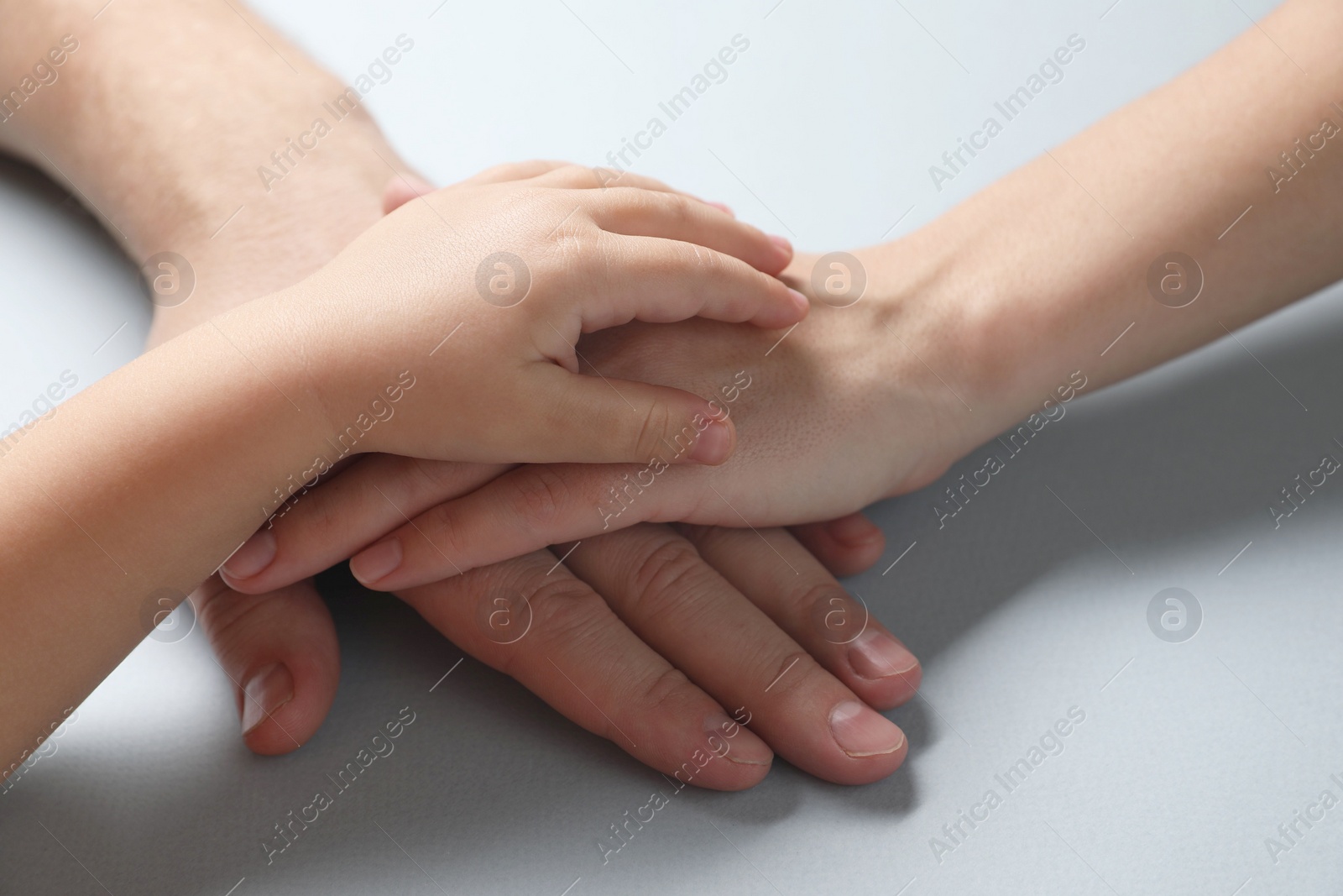 Photo of Parents and child holding hands together on gray background, closeup