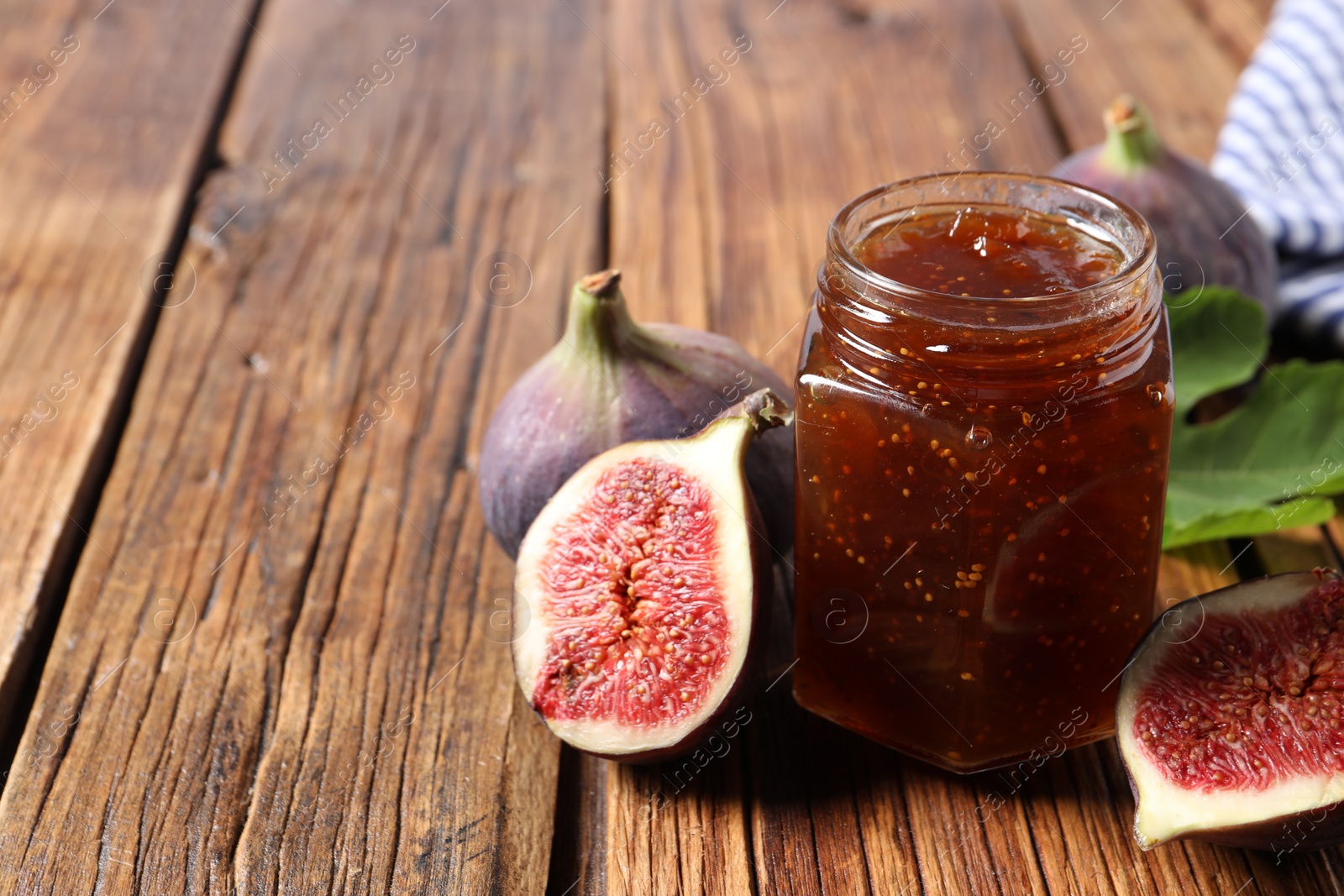 Photo of Jar of tasty sweet jam and fresh figs on wooden table, closeup. Space for text