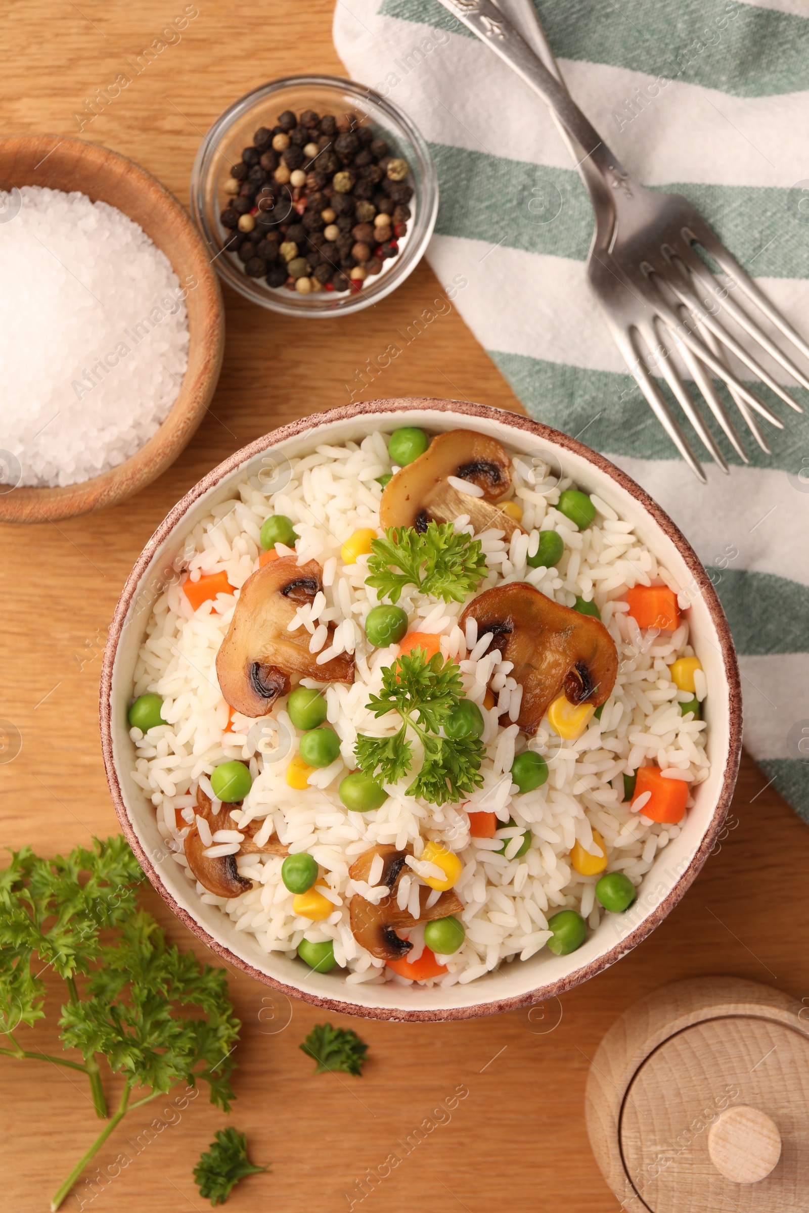 Photo of Bowl of delicious rice with vegetables on wooden table, flat lay
