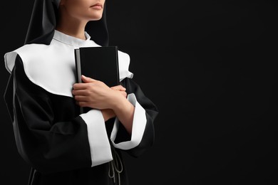 Photo of Nun with Bible on black background, closeup. Space for text
