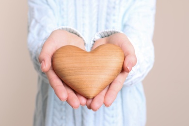 Photo of Young woman holding wooden heart in hands, closeup view