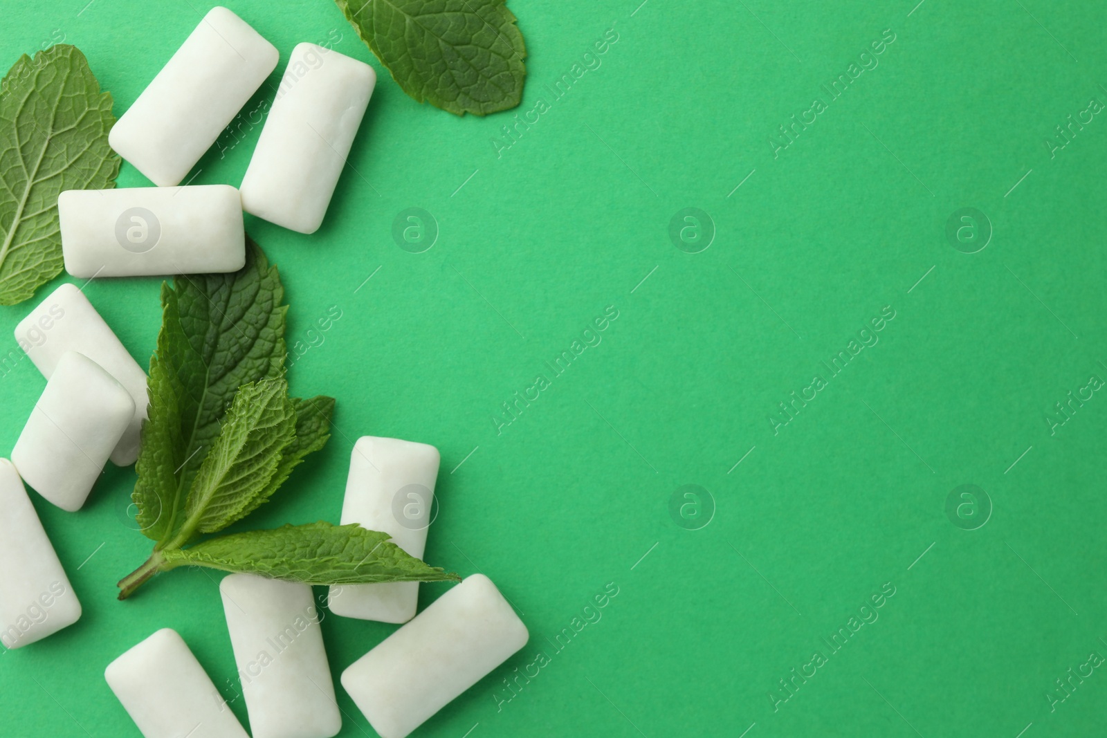 Photo of Tasty white chewing gums and mint leaves on green background, flat lay. Space for text