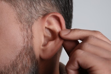 Man touching his ear on light grey background, closeup