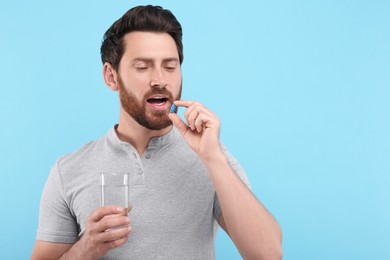 Photo of Handsome man with glass of water taking pill on light blue background, space for text