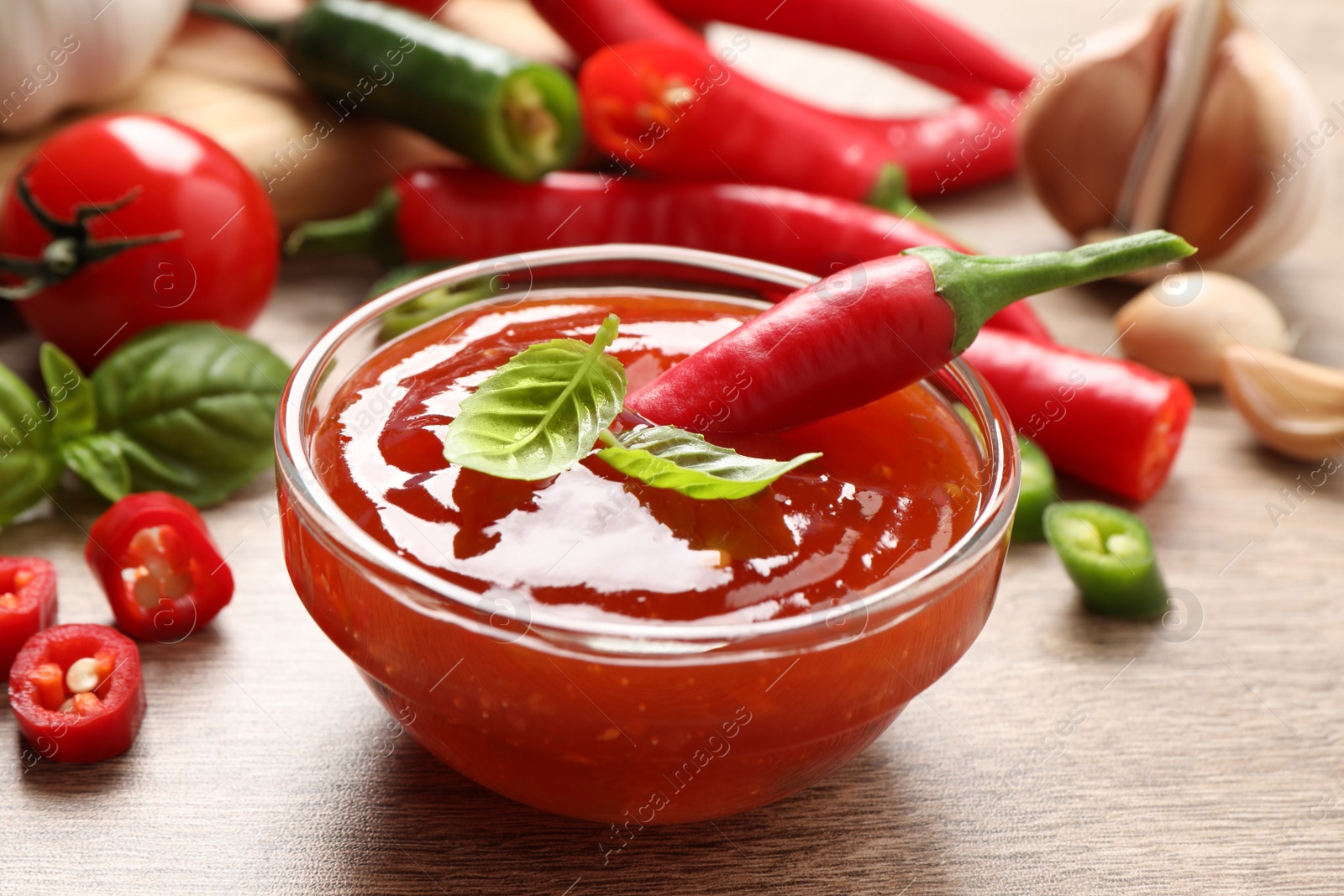 Photo of Spicy chili sauce with basil on wooden table