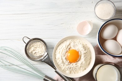 Photo of Flour with yolk in bowl and other ingredients for dough on white wooden table, flat lay