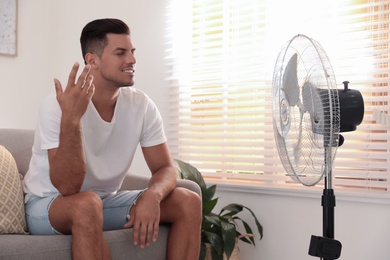 Man enjoying air flow from fan on sofa in living room. Summer heat