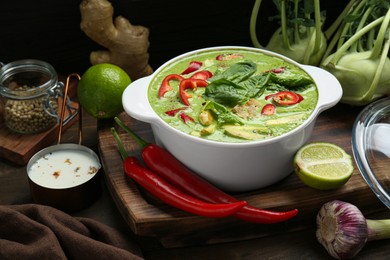 Photo of Saucepan with delicious green curry chicken soup and different ingredients on wooden table