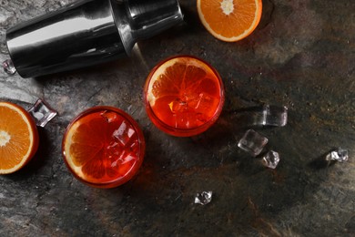 Aperol spritz cocktail, ice cubes and orange slices in glasses and shaker on grey textured table, flat lay