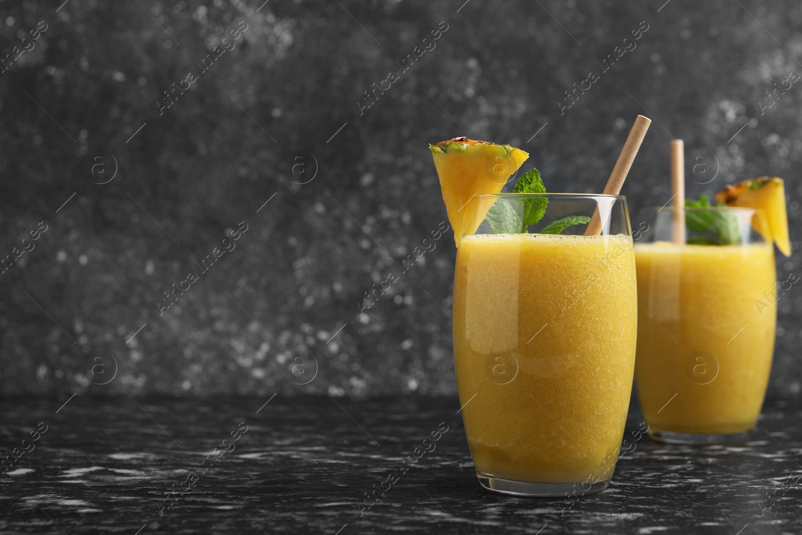 Photo of Tasty pineapple smoothie in glasses on black textured table. Space for text