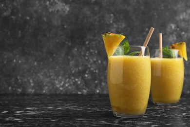 Photo of Tasty pineapple smoothie in glasses on black textured table. Space for text