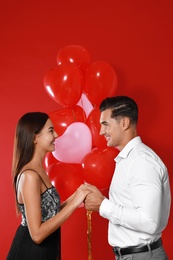 Photo of Beautiful couple with heart shaped balloons on red background