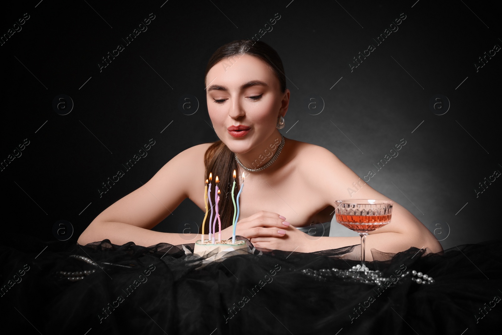 Photo of Fashionable photo of attractive young woman blowing candles on her Birthday cake against black background