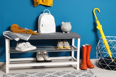 Hallway interior with stylish furniture, shoes and accessories near blue wall