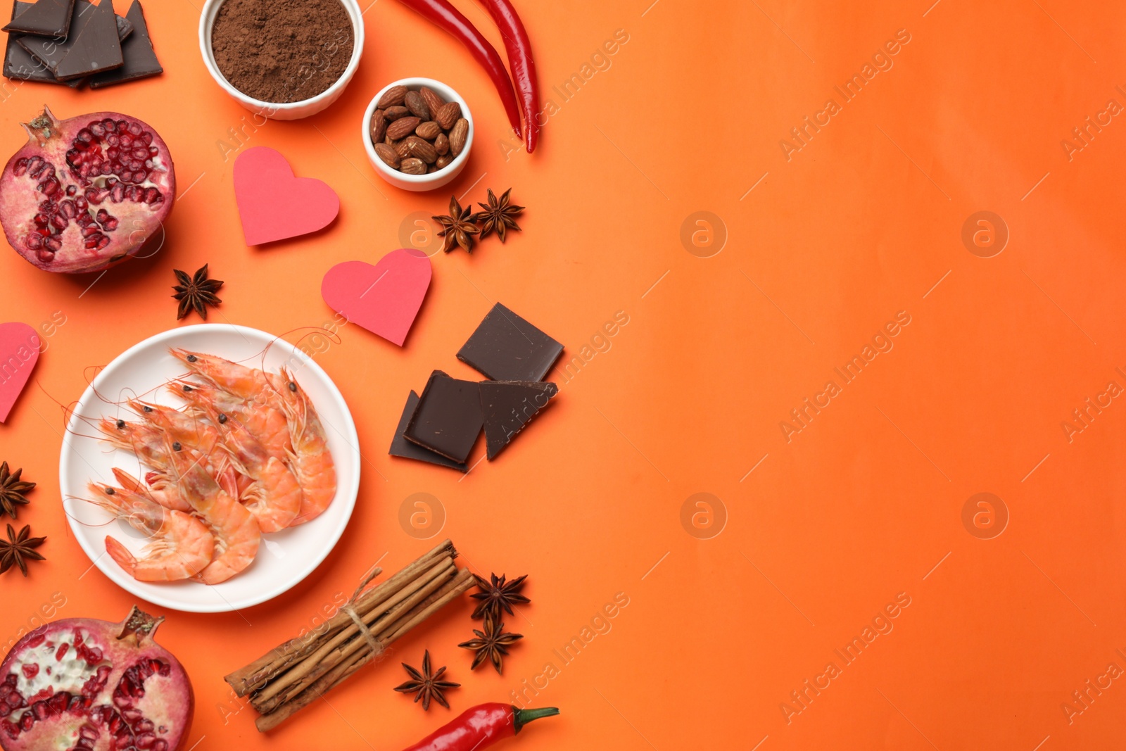 Photo of Natural aphrodisiac. Different products and paper hearts on orange background, flat lay. Space for text