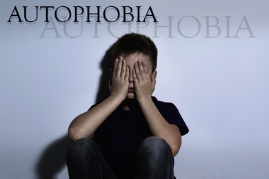 Upset boy closing eyes near white wall. Autophobia - fear of isolation