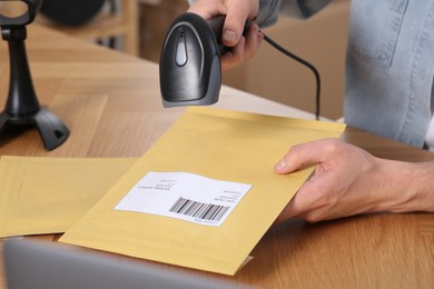 Photo of Seller with scanner reading parcel barcode at table in office, closeup. Online store