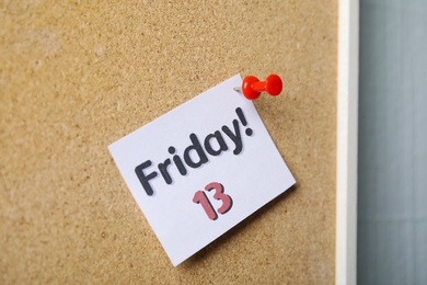 Photo of Paper note with phrase Friday! 13 pinned to cork 
board. Bad luck superstition