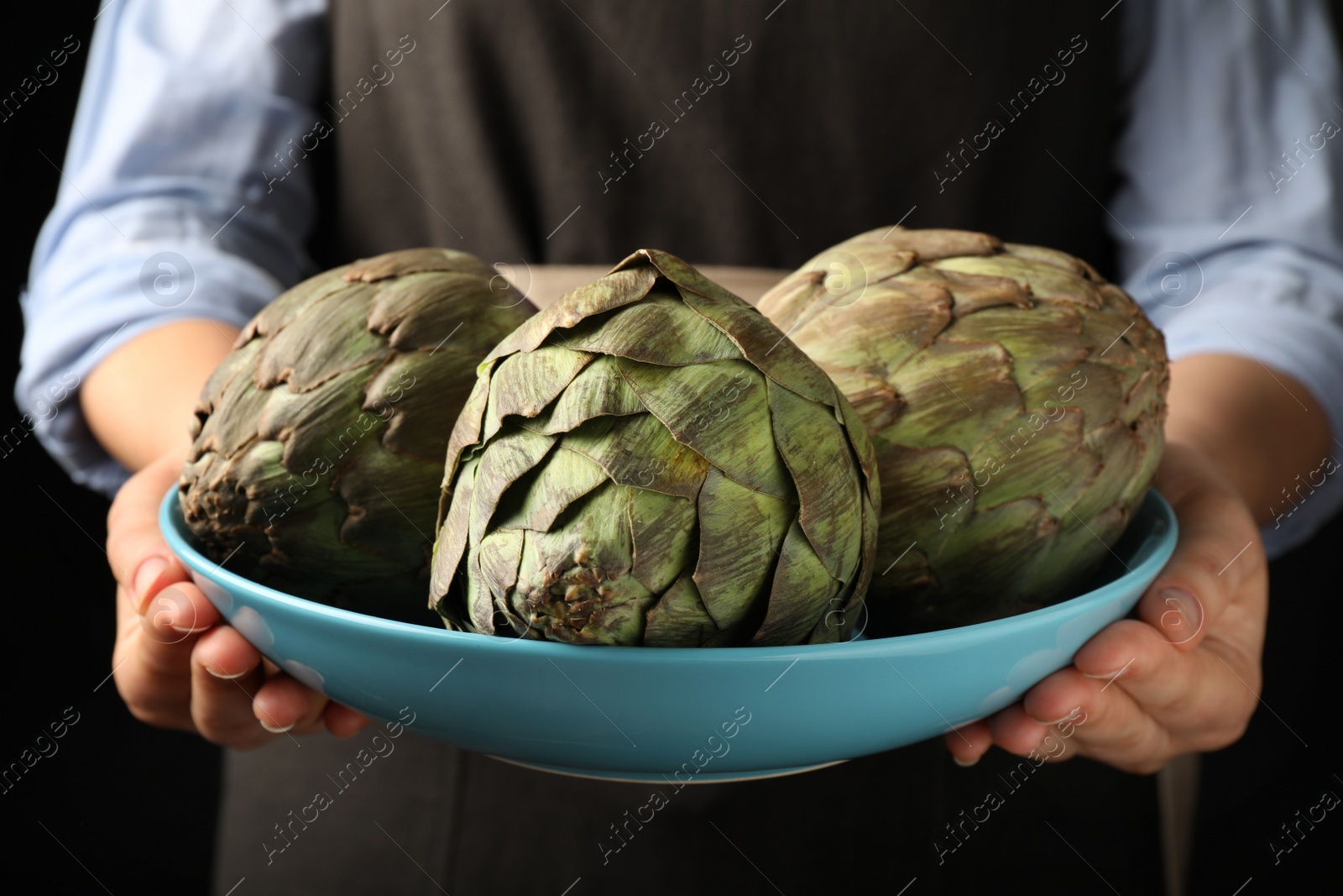 Photo of Woman holding bowl with fresh raw artichokes, closeup